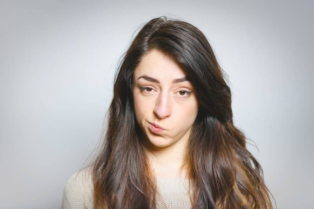 A woman with long dark hair looking at the camera with a skeptical or annoyed facial expression.