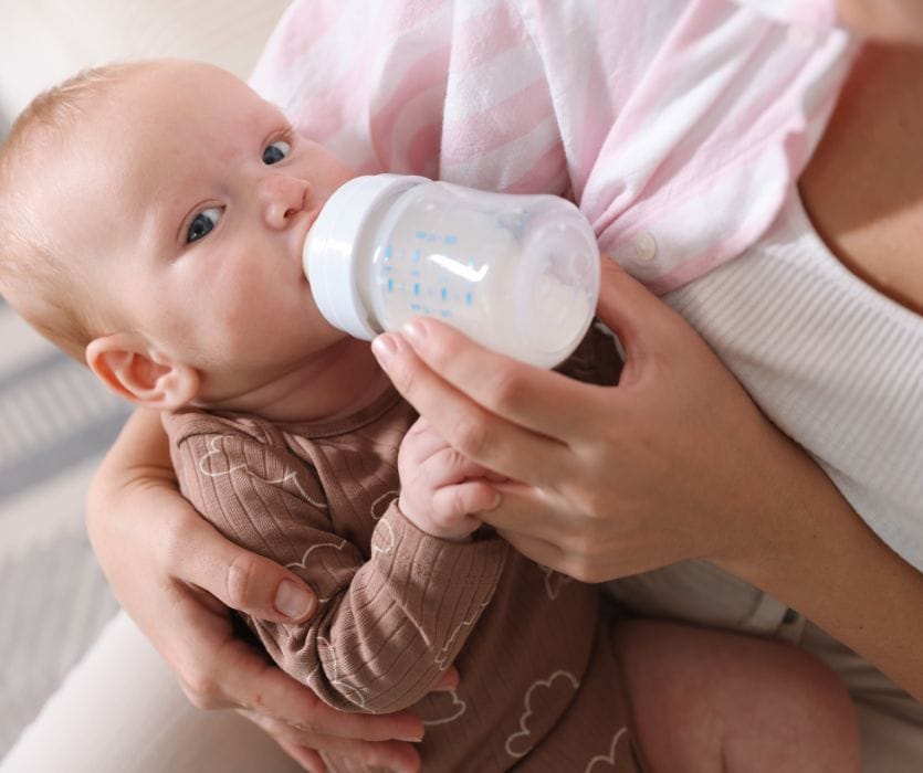 A person cradling a baby while bottle-feeding them with infant formula.