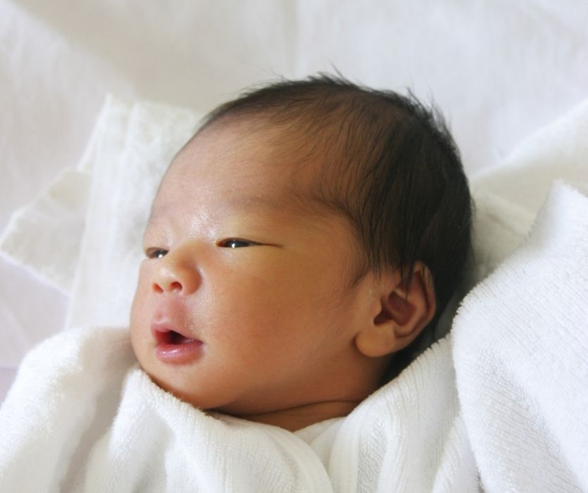 Newborn baby with dark hair wrapped in a white blanket.