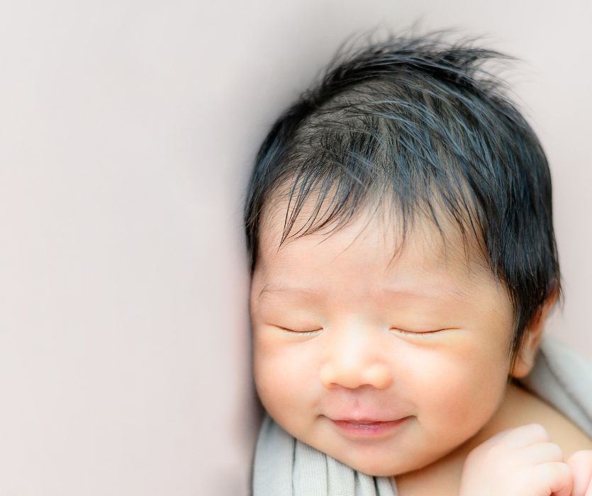 Close-up of a sleeping newborn with dark hair and a slight smile.