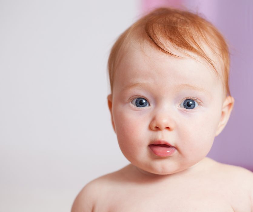 Close-up of a baby with blue eyes and short, thin reddish-blonde hair brushed to the side.