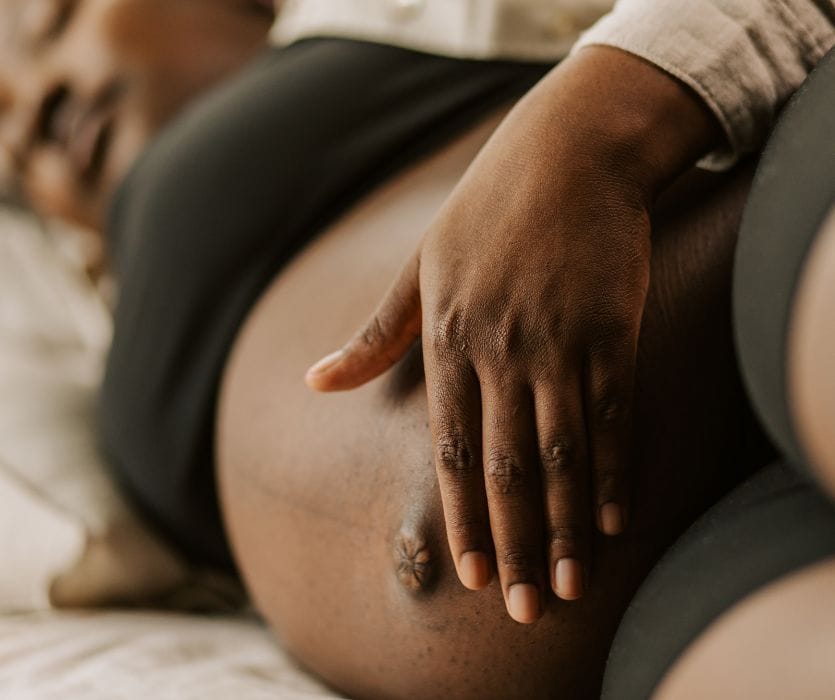 Close-up of a person with dark skin resting their hand on their pregnant belly.