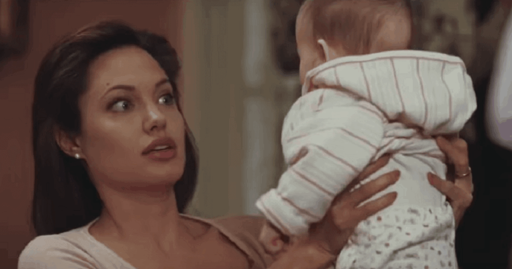 Angelina Jolie looks surprised while holding a baby wearing a striped hooded sweater.