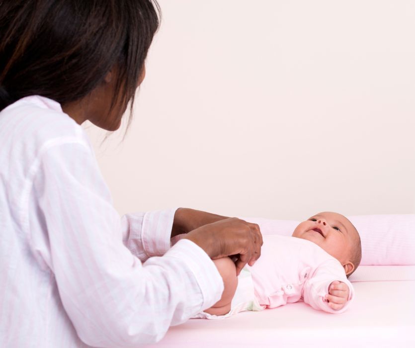 Close-up of a mother changing her smiling baby’s diaper on a pink surface.