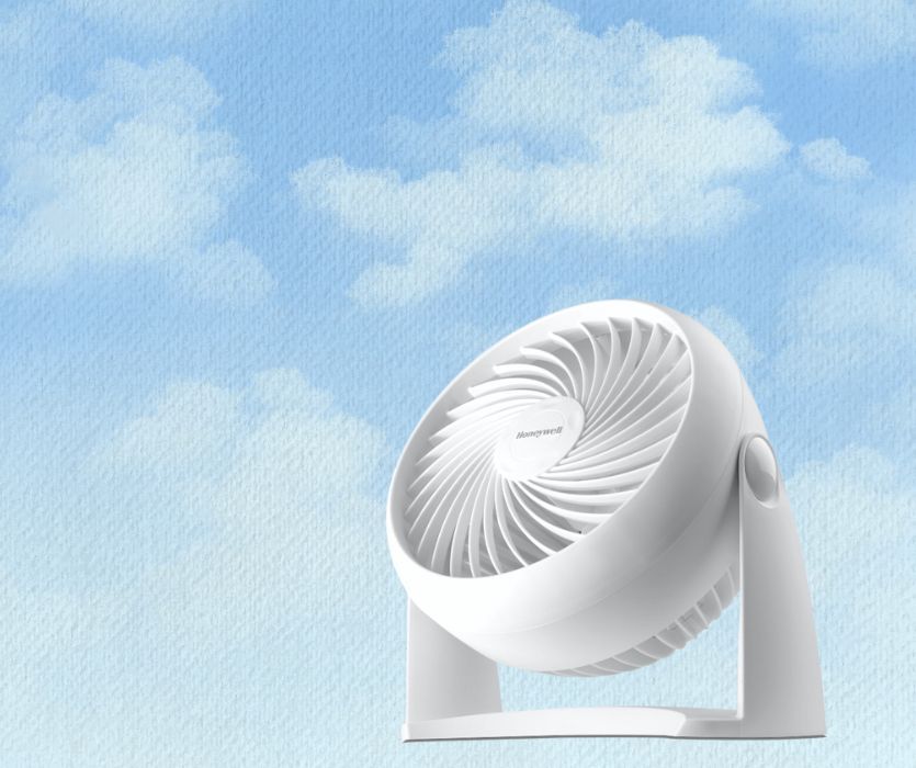 White Honeywell TurboForce desk fan positioned against a light blue sky background with painted clouds.