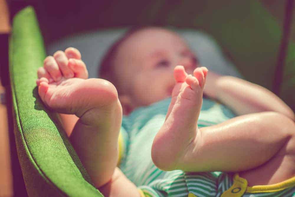 Close-up of a baby's feet as they lie on their back in a green cushioned seat.
