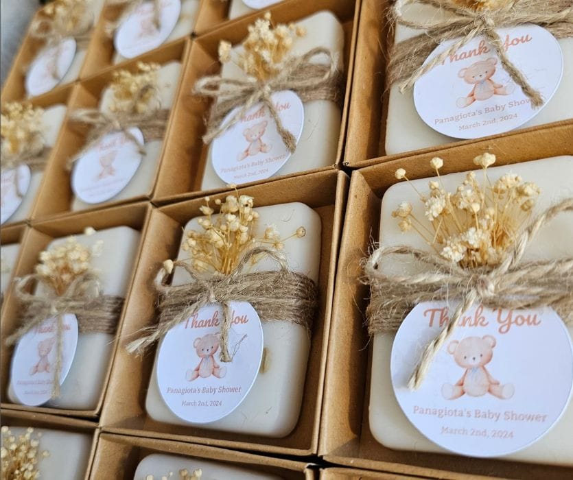 Neatly boxed baby shower favors feature teddy bear thank-you labels, twine bows, and dried flower sprigs.