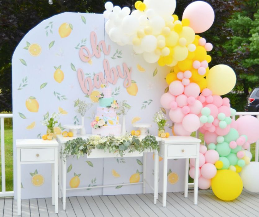 Lemon-themed baby shower backdrop with Oh Baby sign, floral cake, and pink, yellow, and green balloon garland.
