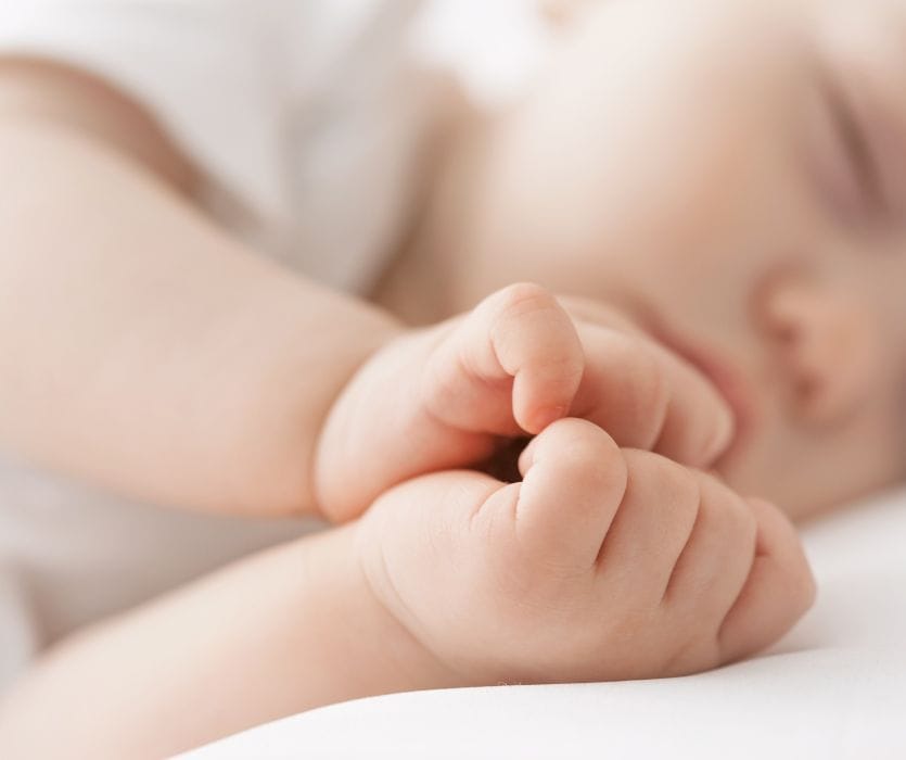 Extreme close-up of a sleeping baby's hands curled together near their face.