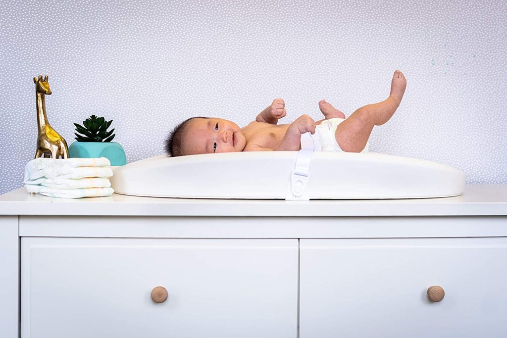 A baby lying on a Hatch Grow Smart Changing Pad and Scale on top of a dresser.