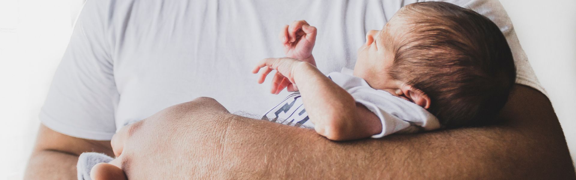 A newborn baby with brown hair being cradled in an adult's arms.