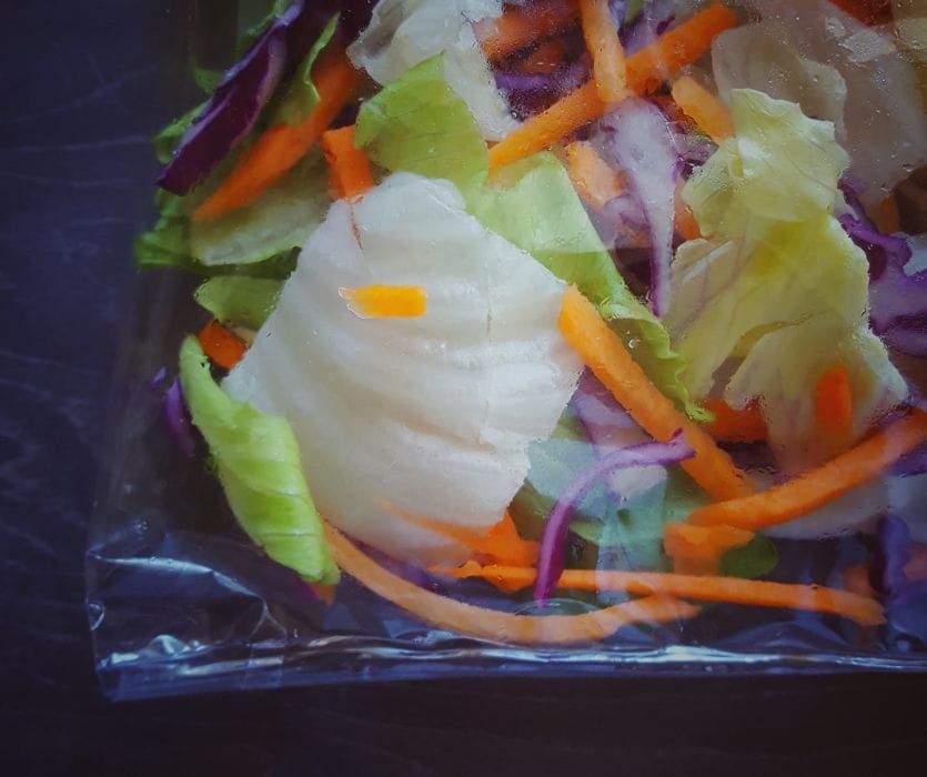 Close-up of a plastic bag filled with shredded carrots, red cabbage, and green lettuce.