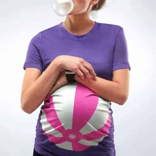 Pregnant person wearing a purple maternity t-shirt featuring a pink and white beach ball graphic over the baby bump.