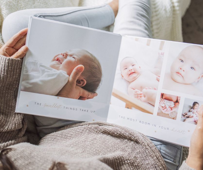 A person holds an open baby photo book featuring portraits and the quote: The smallest things take up most room in your heart.