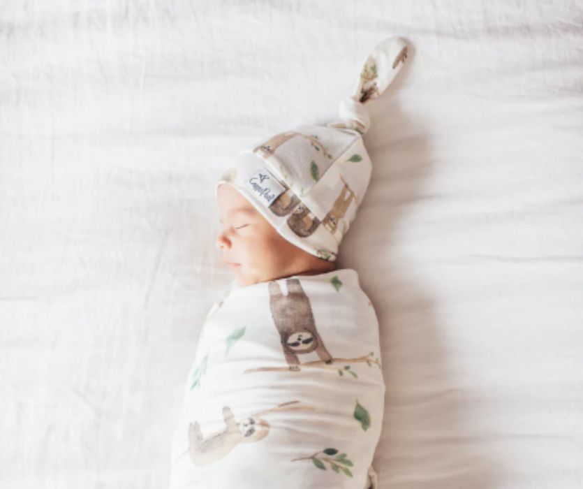 Sleeping newborn wrapped in a sloth-patterned swaddle and matching top-knot hat.
