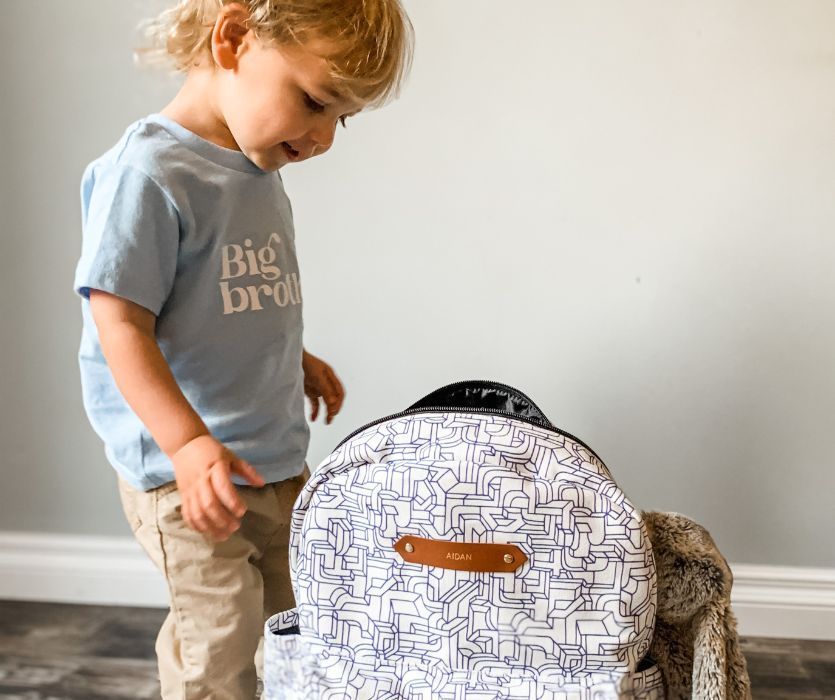 A young boy wearing a Big Brother t-shirt looking down at a personalized geometric pattern backpack.