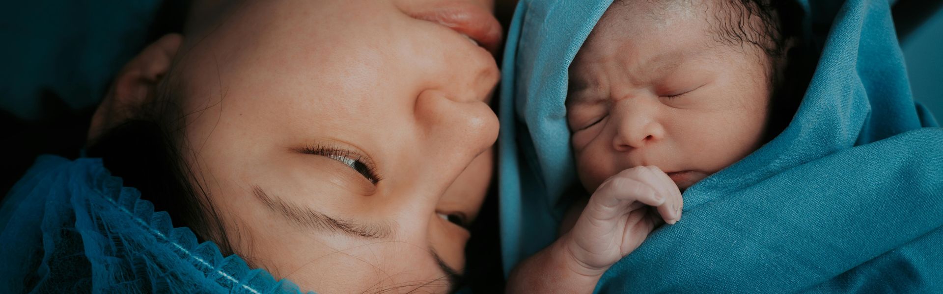 Close-up of a mother looking at her newborn baby wrapped in a blue blanket.
