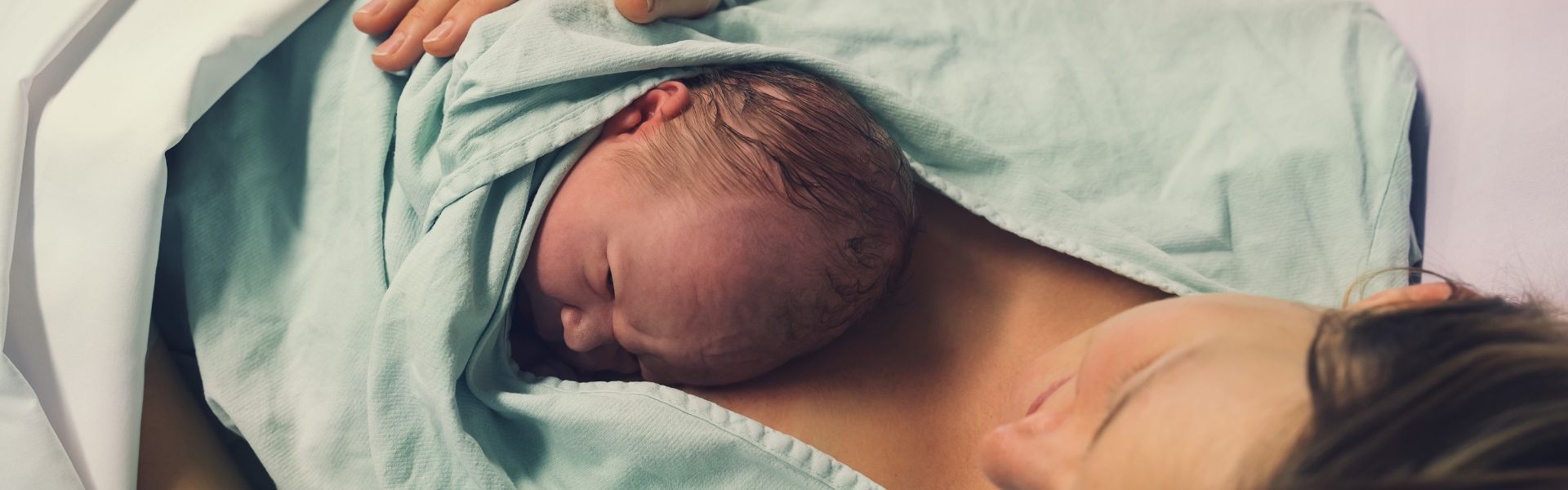 A newborn baby with wet hair rests on a mother's bare chest for skin-to-skin contact after birth.