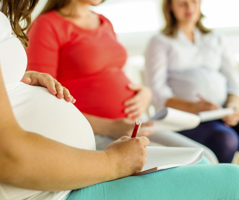 Three pregnant women sitting in a row taking notes on paper at a birthing class.