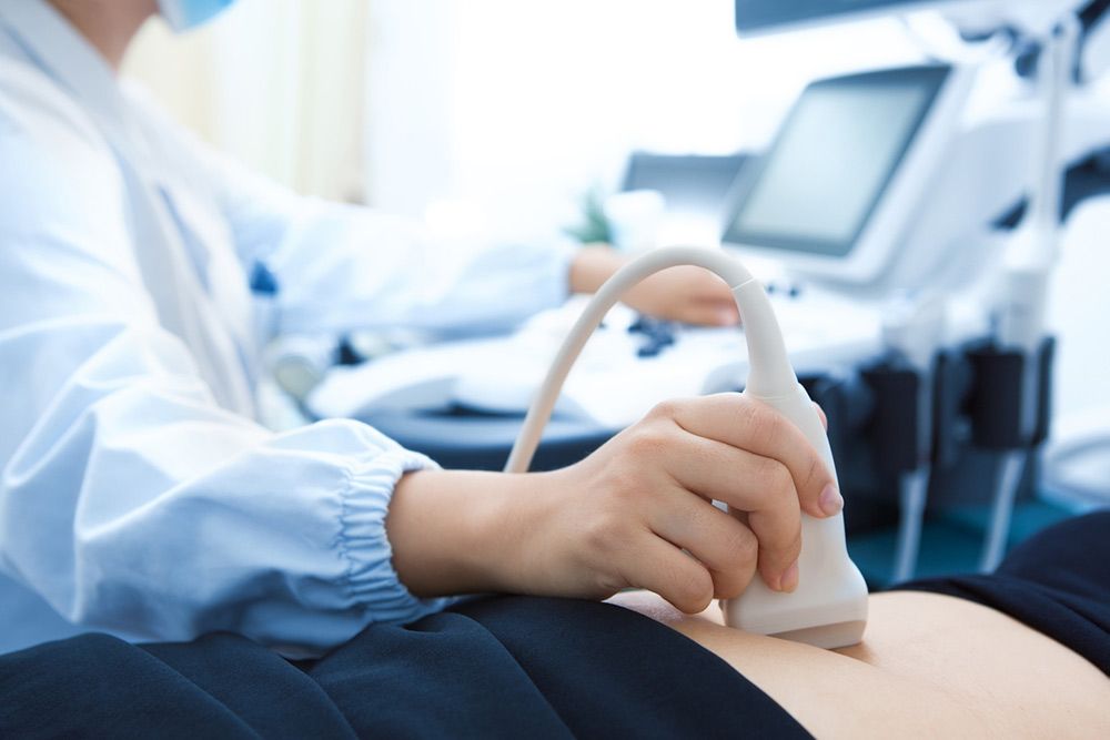 A medical professional uses an ultrasound transducer on a patient's abdomen in a clinical setting.