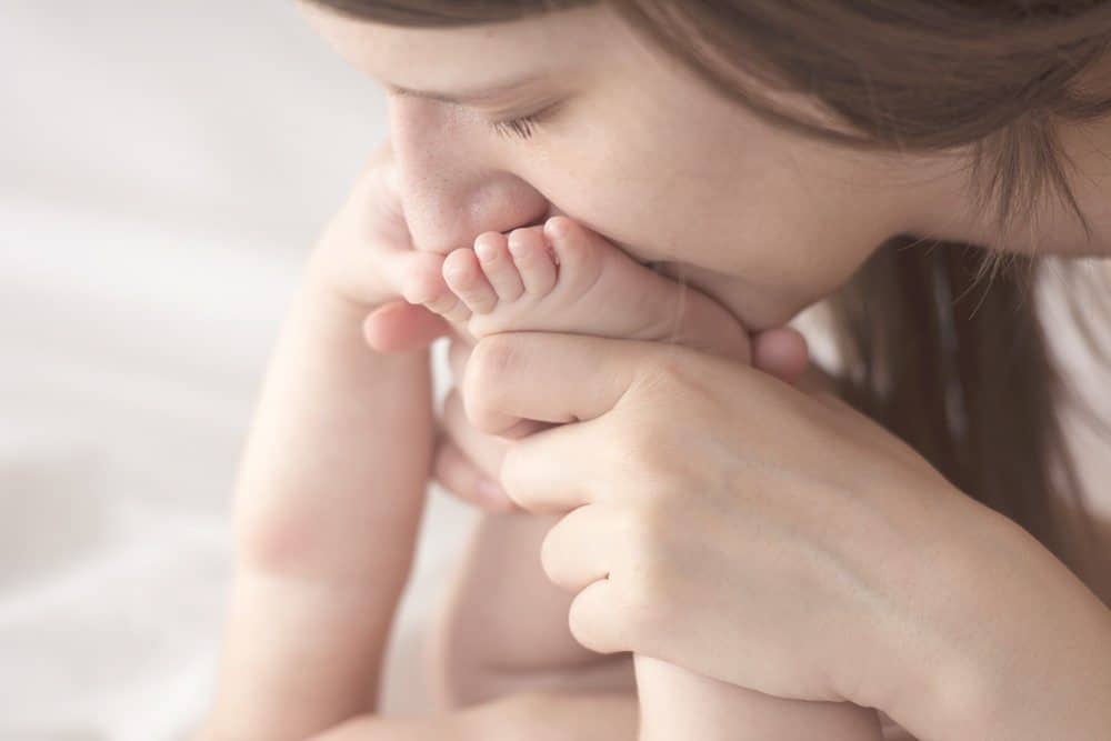 Close-up of a mother kissing her baby's foot while holding it with both hands.