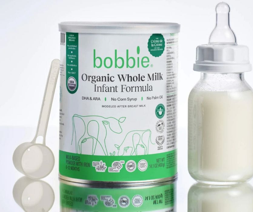 Bobbie Organic Whole Milk Infant Formula can next to a plastic scoop and a prepared baby bottle.