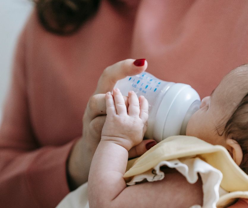 Close-up of a person holding a plastic bottle while a baby drinks from it.