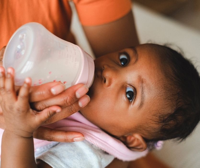 Close-up of a baby drinking from a pink bottle held by an adult.