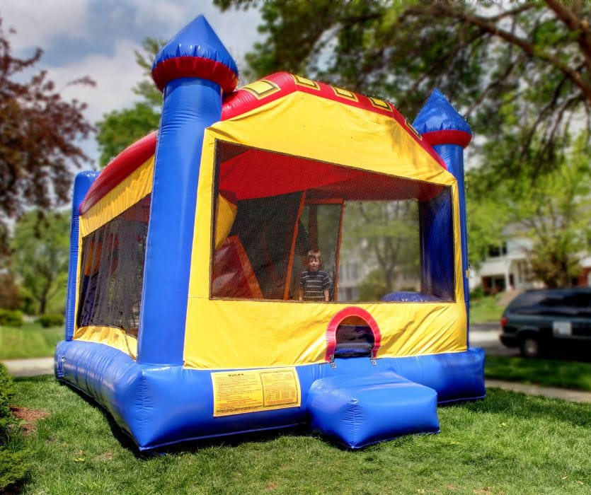 A colorful blue, yellow, and red inflatable bouncy castle on a residential lawn with a child visible inside.