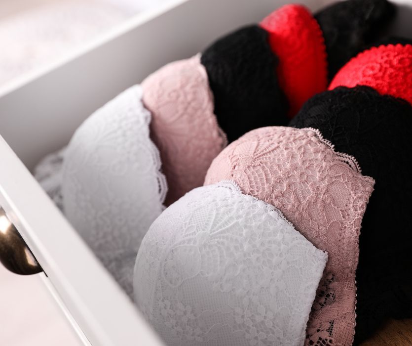 Various lace bras in white, pink, black, and red neatly folded inside a white dresser drawer.