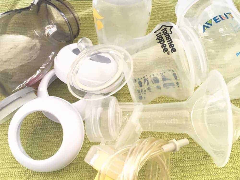 Disassembled breast pump parts, including bottles, flanges, and tubing, drying on a green textured towel.