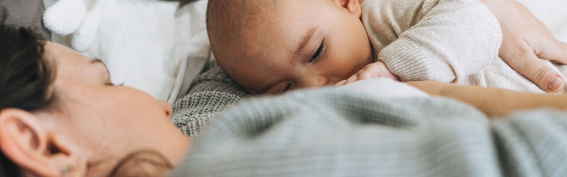 Close-up of a mother breastfeeding her infant while lying down in bed.