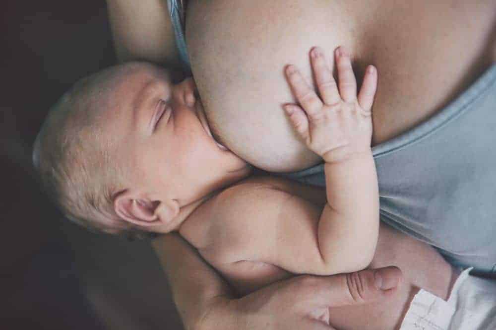 Close-up of a newborn infant breastfeeding with their hand resting on the mother's chest.