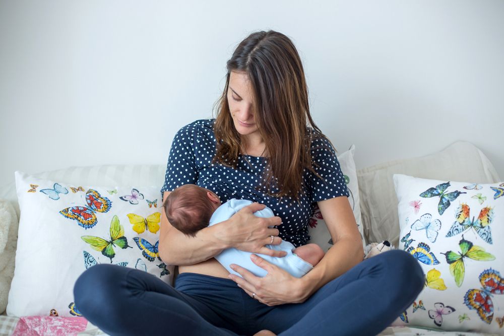 A mother sitting on a couch among butterfly pillows breastfeeding her newborn baby.