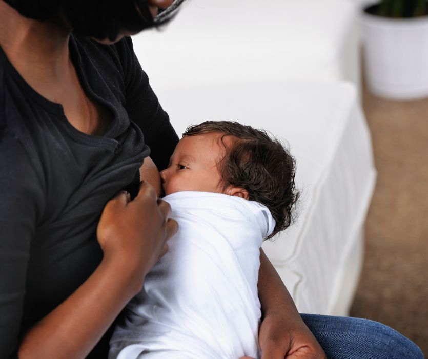 A mother holding and breastfeeding an infant swaddled in a white blanket.