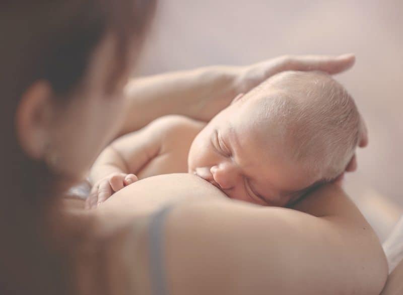 A newborn baby breastfeeding while being cradled by a mother.