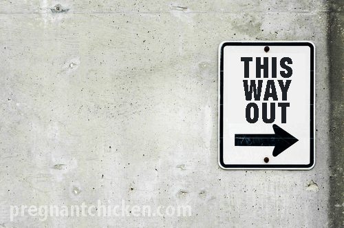 A white sign on a concrete wall with black text reading THIS WAY OUT above a right-pointing arrow.