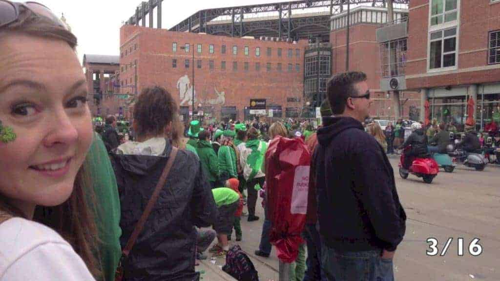 Close-up of a smiling woman near a crowded street with people in green for a St. Patrick's Day parade.
