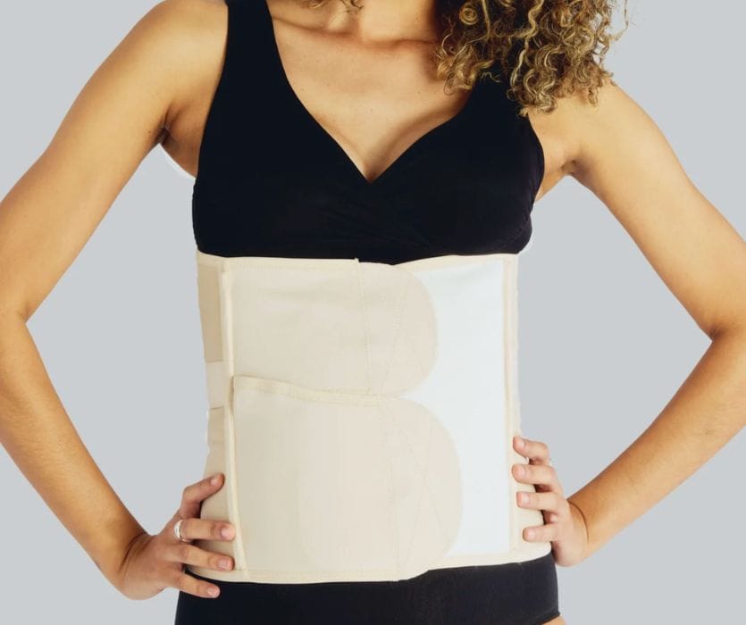 Woman wearing a tan abdominal compression girdle over a black tank top and leggings.