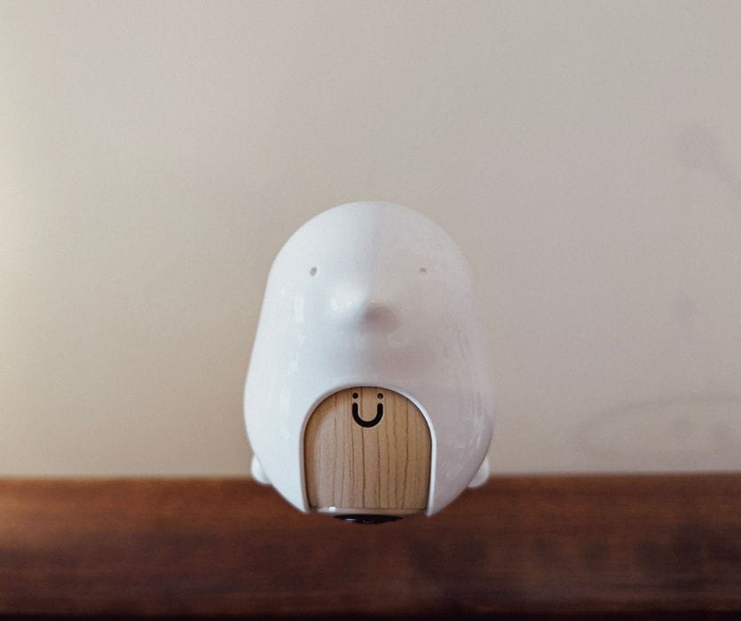 Cubo Ai baby monitor shaped like a white bird with a wood-grain face and a small camera lens.