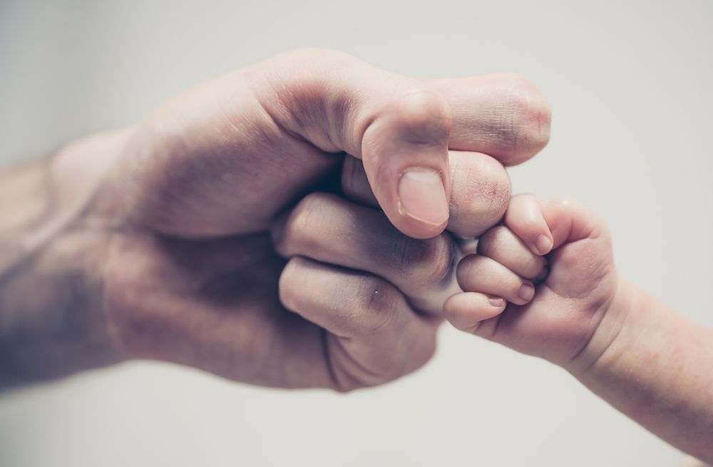 Close-up of an adult's fist and a baby's tiny fist meeting in a fist bump.