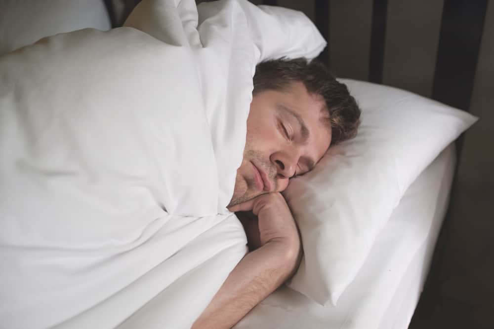 A man sleeping soundly in a bed with white linens.