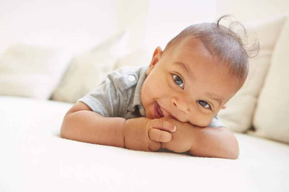 Smiling baby lying on their stomach during tummy time, resting their chin on their hands.