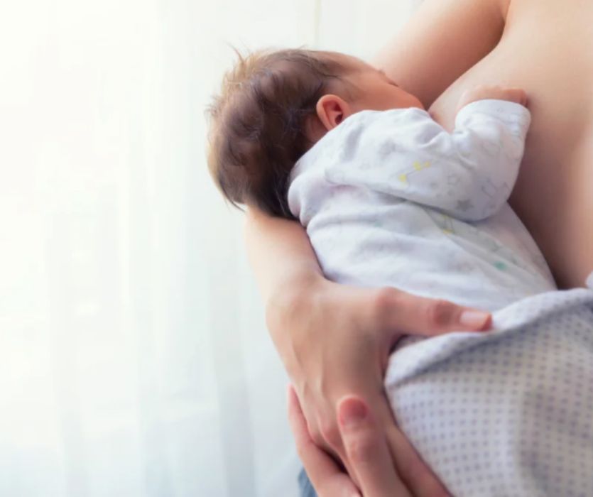 A woman cradling and breastfeeding a newborn baby in a white patterned onesie.