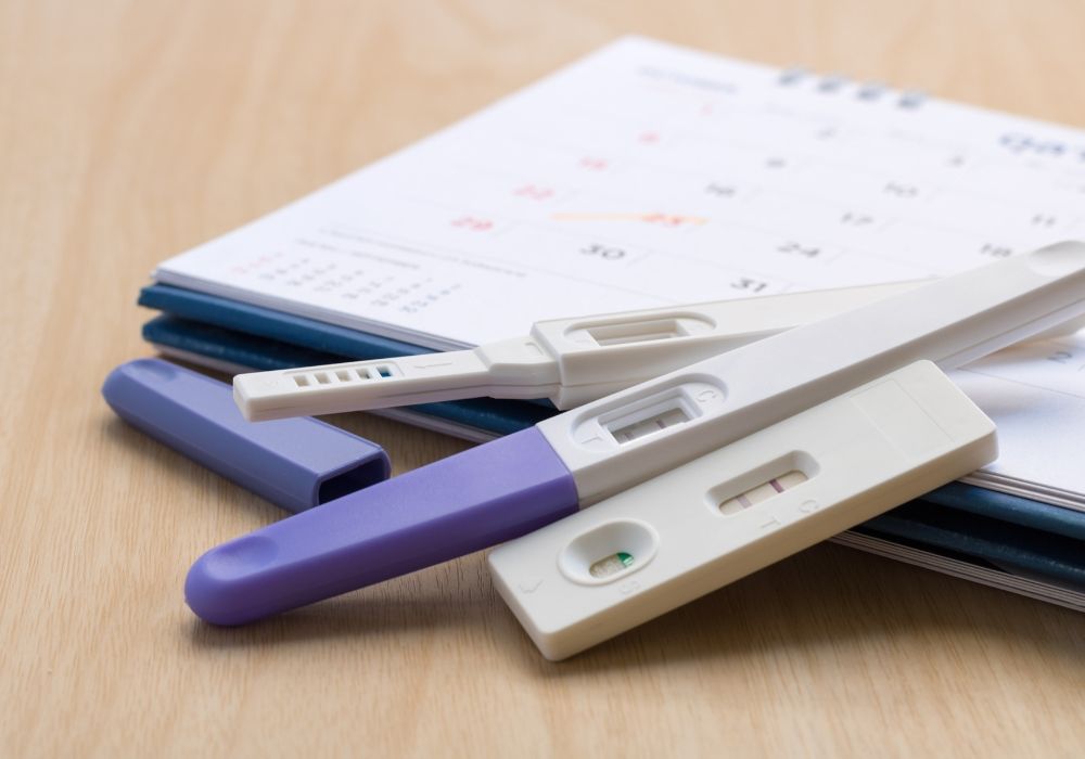 Three pregnancy test sticks with single lines resting on a paper desk calendar.