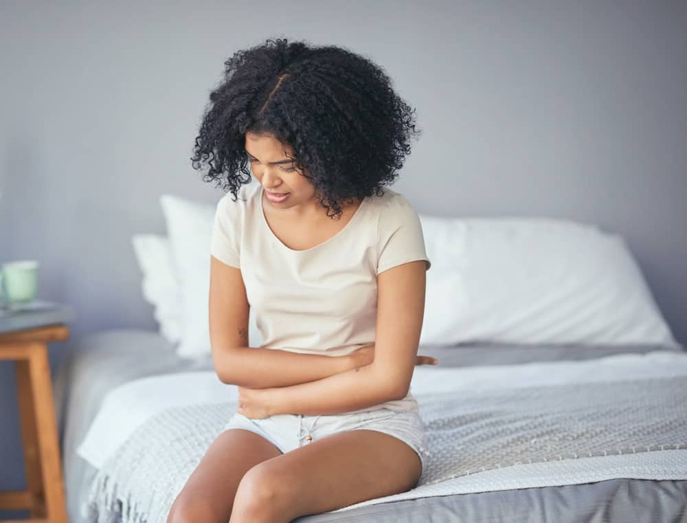 A woman sitting on a bed clutching her abdomen in pain, illustrating potential symptoms of an ectopic pregnancy.