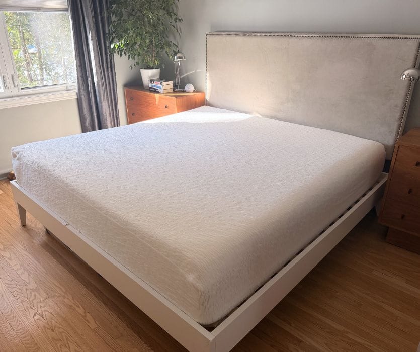 White Endy mattress on a platform bed frame with a grey tufted headboard in a bright bedroom.