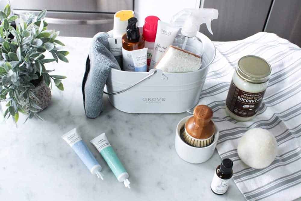 Cleaning supplies in a white Grove caddy, including bottles, a scrub brush, and tubes on a marble countertop.