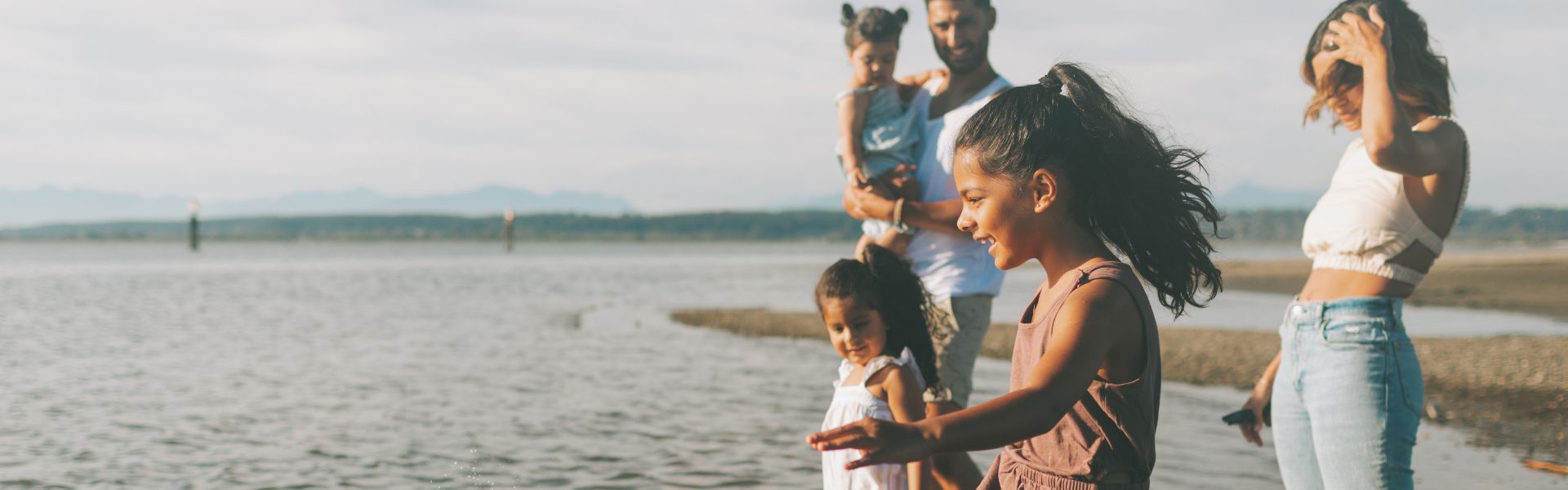 A family with three children spends time standing on a beach at the water's edge.