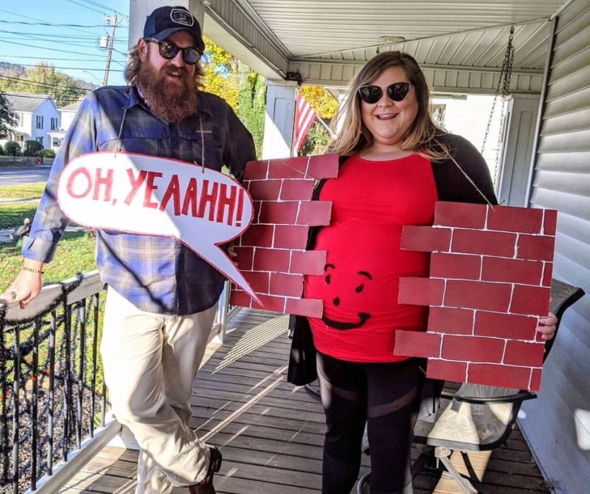 A couple in a Kool-Aid Man and brick wall maternity Halloween costume on a porch.